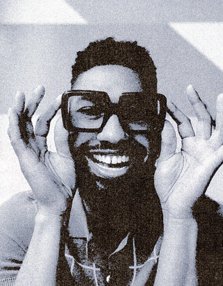 A woman with long brown hair lying on a bed, wearing a white robe, holding up her hand in a peace sign gesture, and smiling at the camera.
