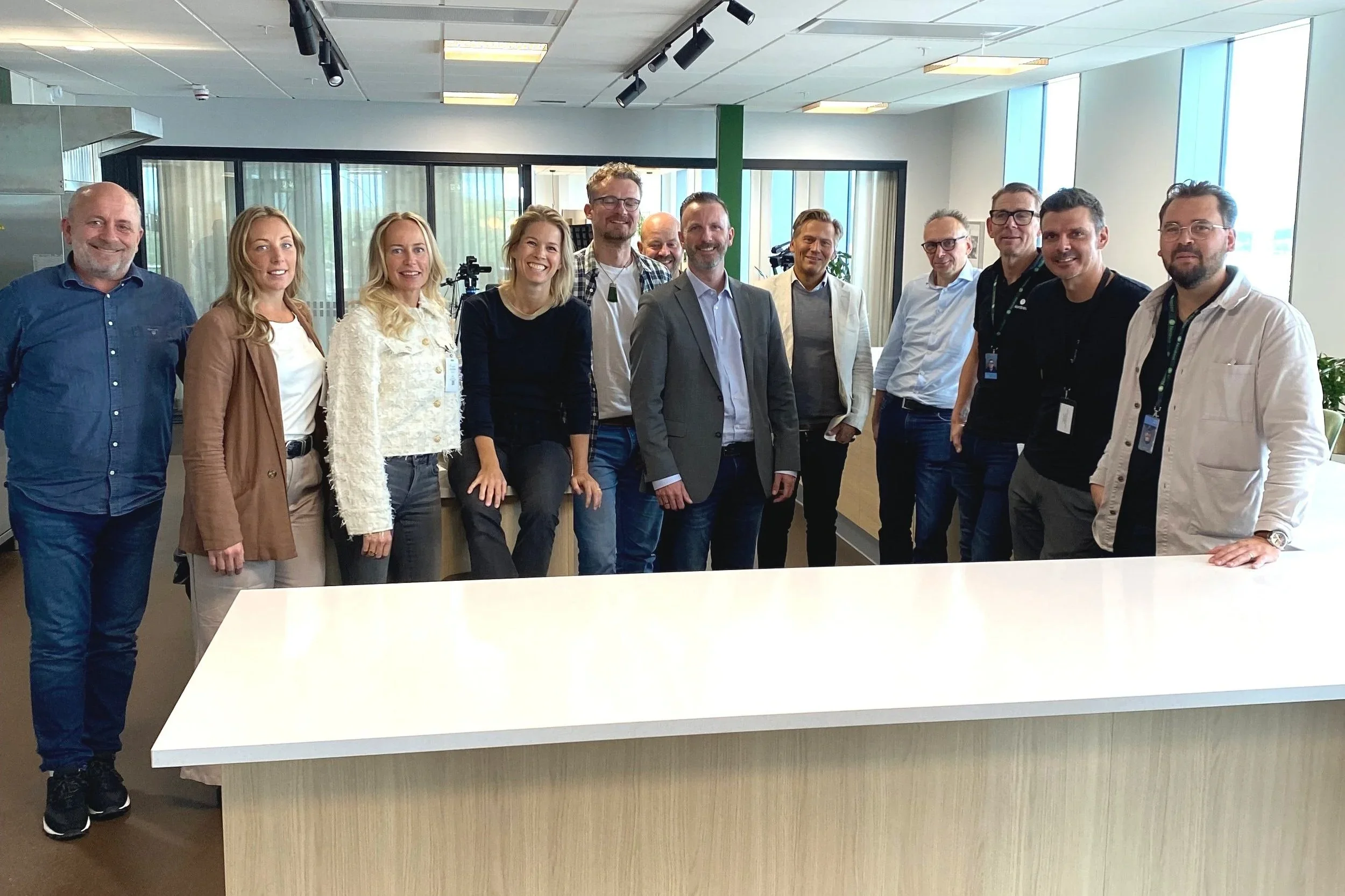 Grupp av personer som stÄr ihop i ett kontorslandskap, alla ler och ser nöjda ut.