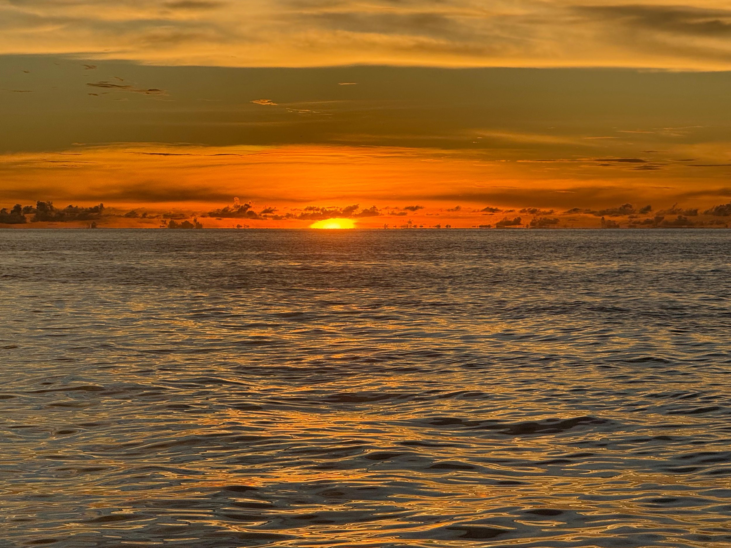 Sunset over the ocean with orange and yellow hues in the sky and gentle waves on the water.