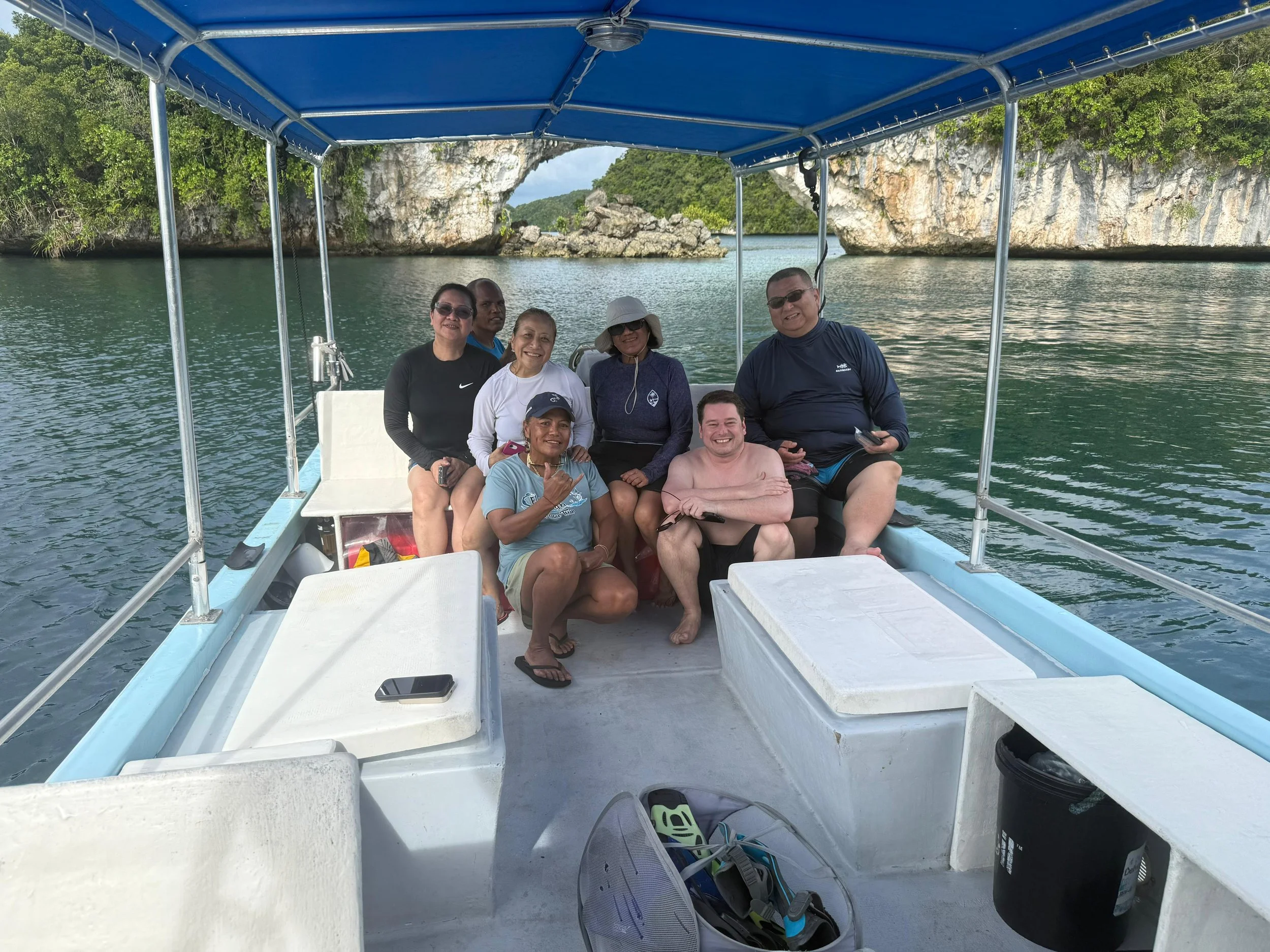 Group of seven people on a boat with rocky island and water in the background.