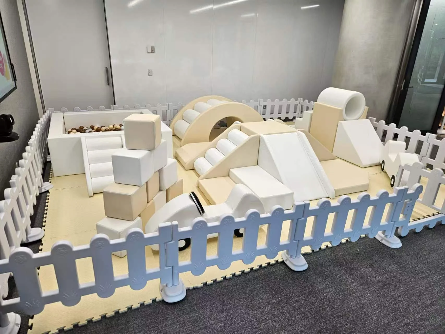 Indoor play area for children with soft foam blocks and tunnels surrounded by a white picket fence.