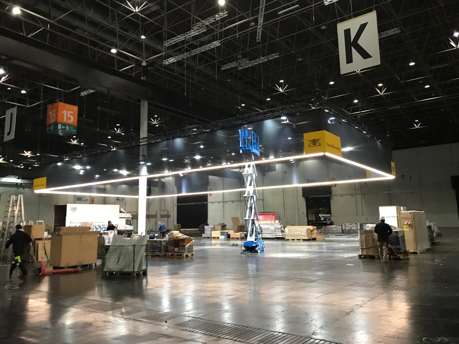 Large black hanging structure with integrated lighting being installed in an indoor space, with workers and equipment around.