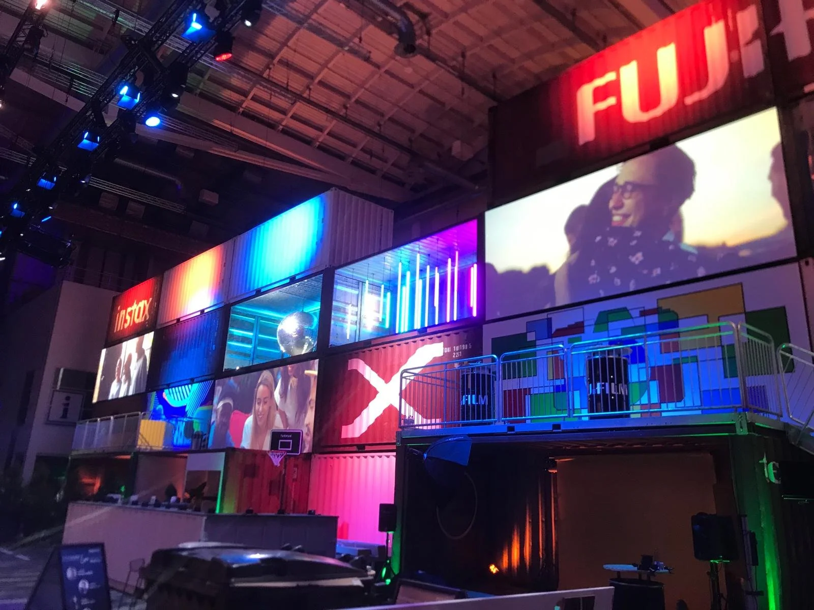 Interior of a vibrant event space with multiple large screens displaying colorful visuals and text that includes 