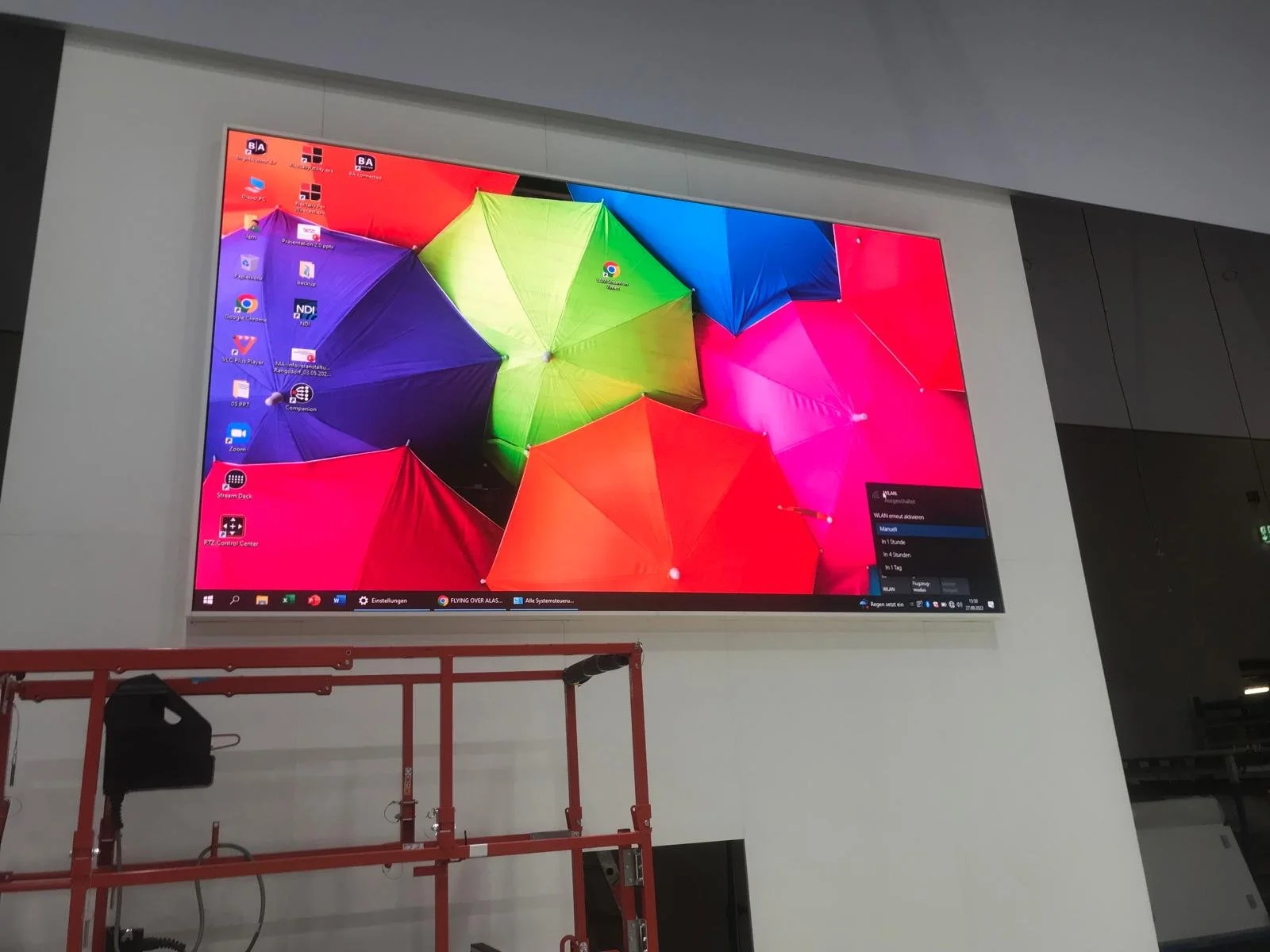 A large screen displays a vibrant background of overlapping umbrellas in red, yellow, green, blue, purple, and pink, with some computer icons and a menu overlay on the right side.