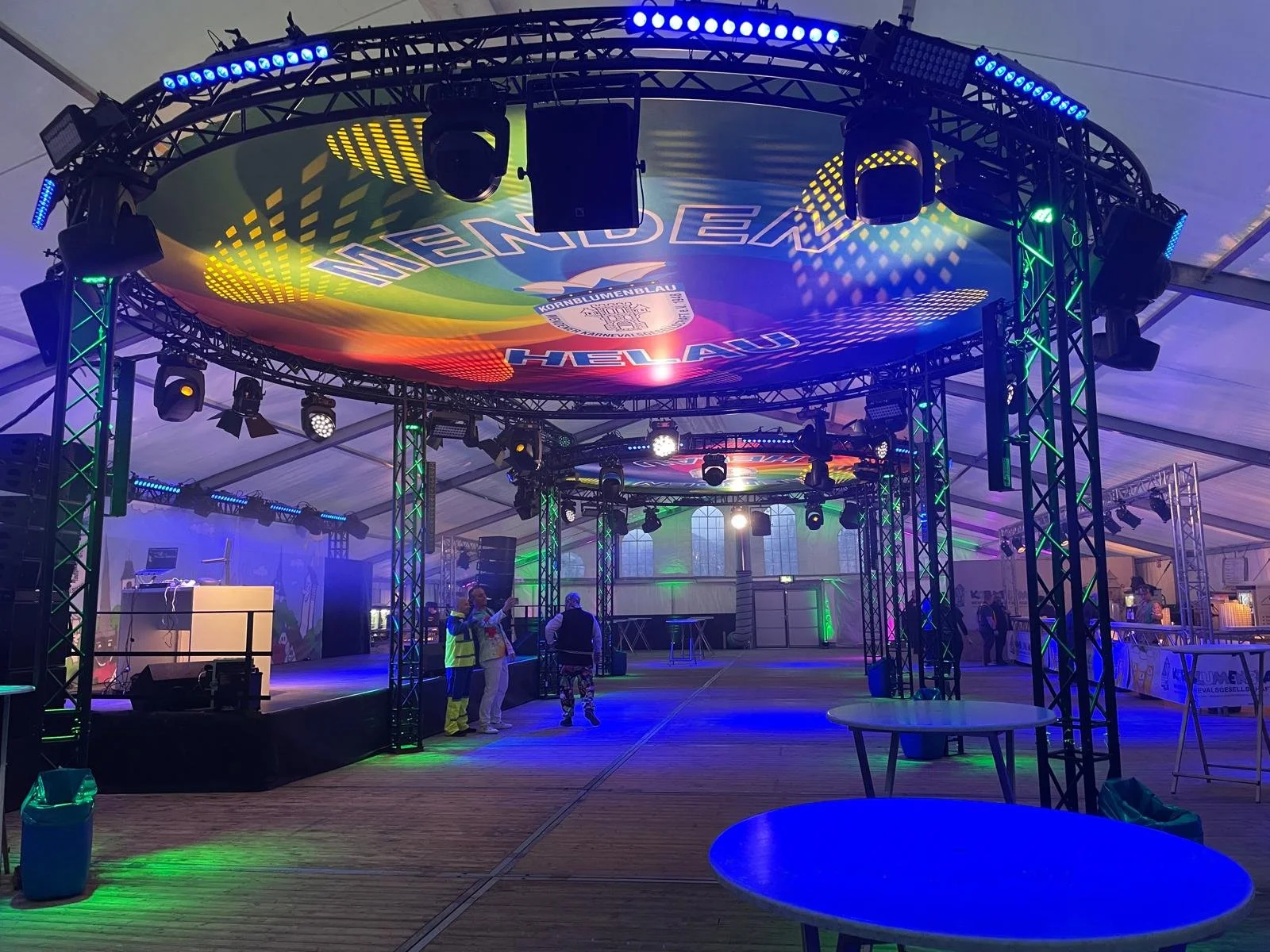 Empty event tent with a brightly lit stage, colorful LED lights, and a large circular sign overhead that reads 'NEMO' and 'HELLAU'.