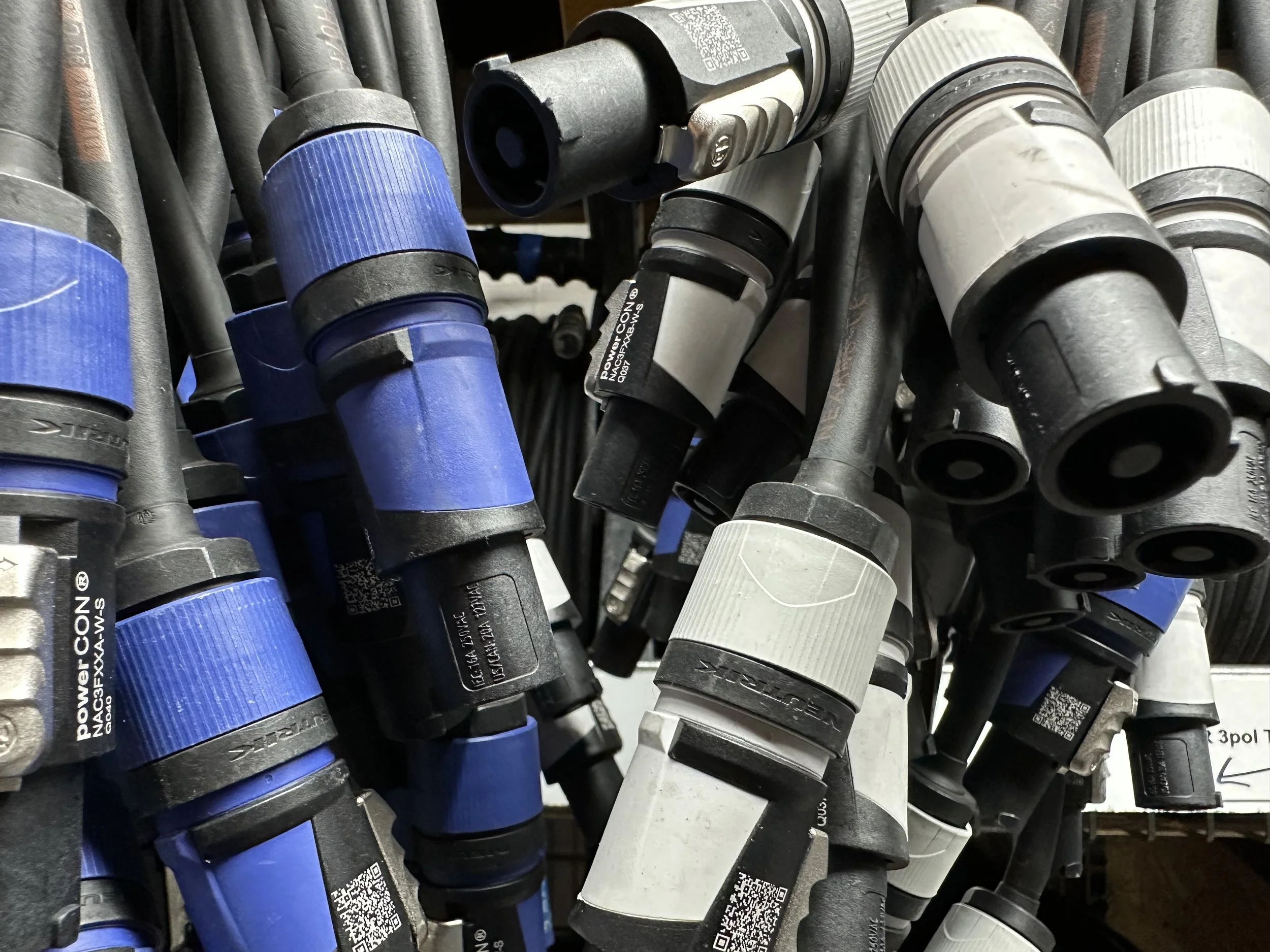 Assorted electrical connectors and cables, including blue and gray plugs with QR codes, hanging in a workshop or hardware store.