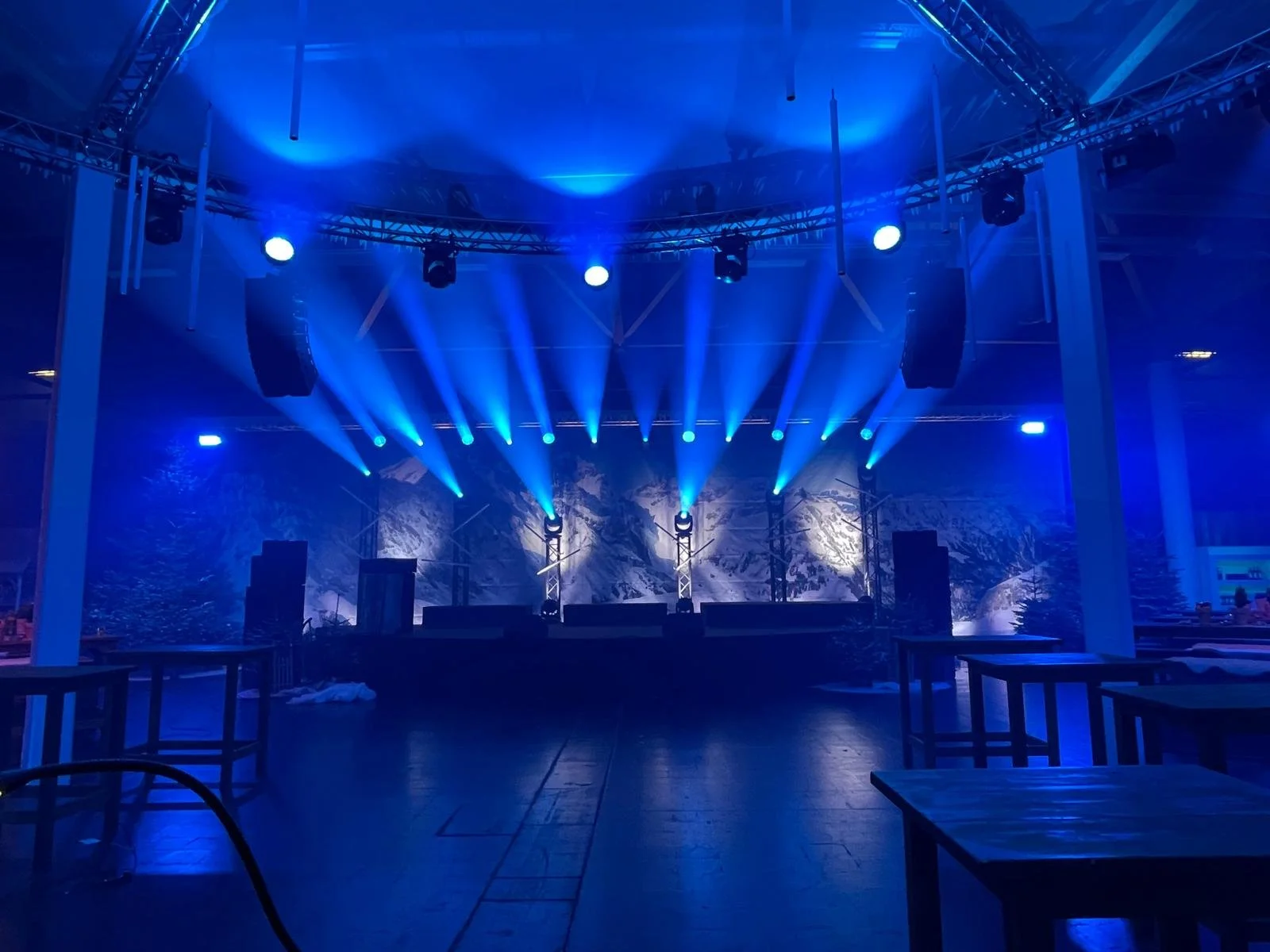 Empty indoor stage with blue lighting, spotlights, and a mountain landscape backdrop.