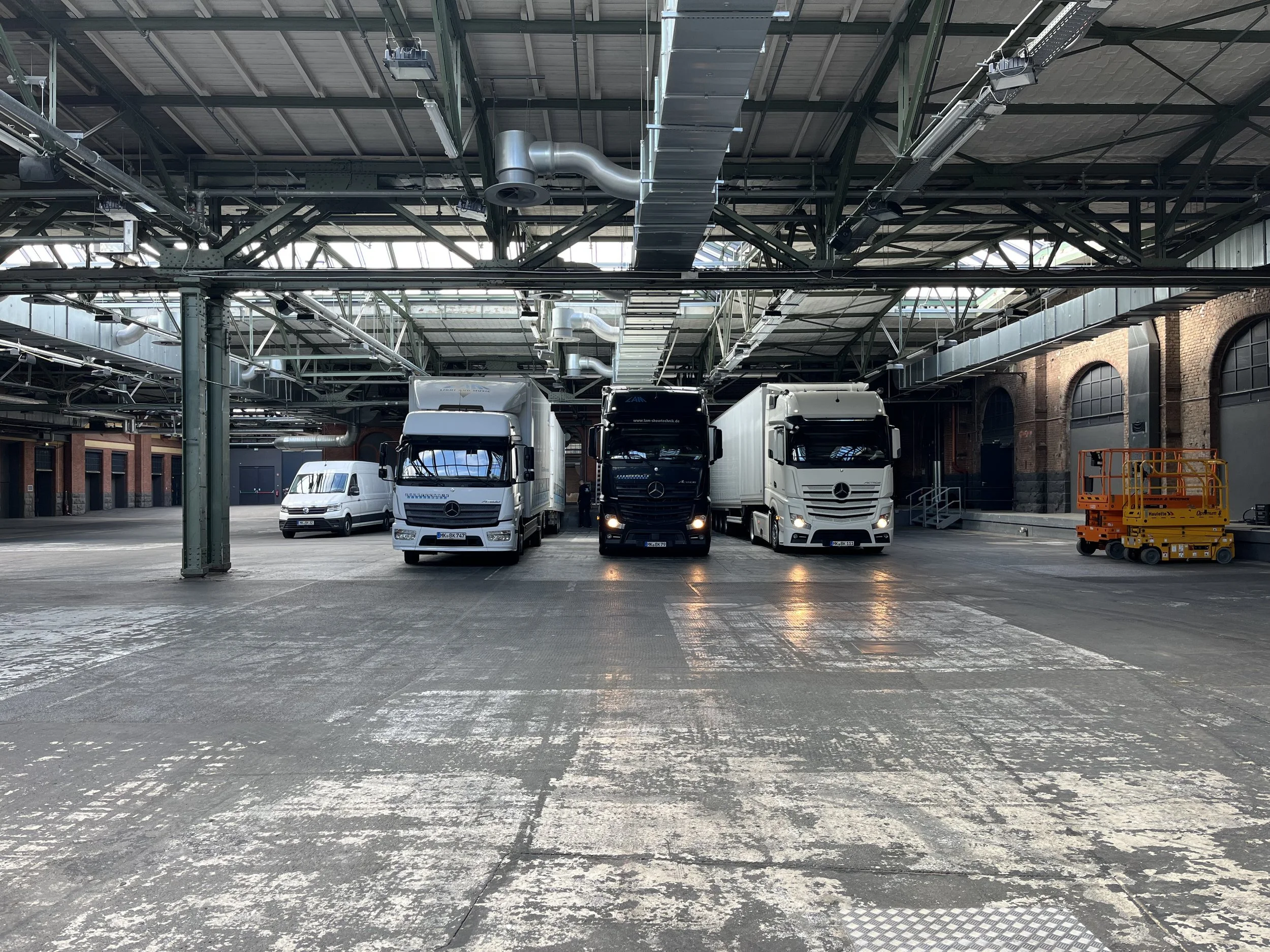 Three trucks and a van parked inside a large industrial warehouse with exposed metal beams and brick walls.