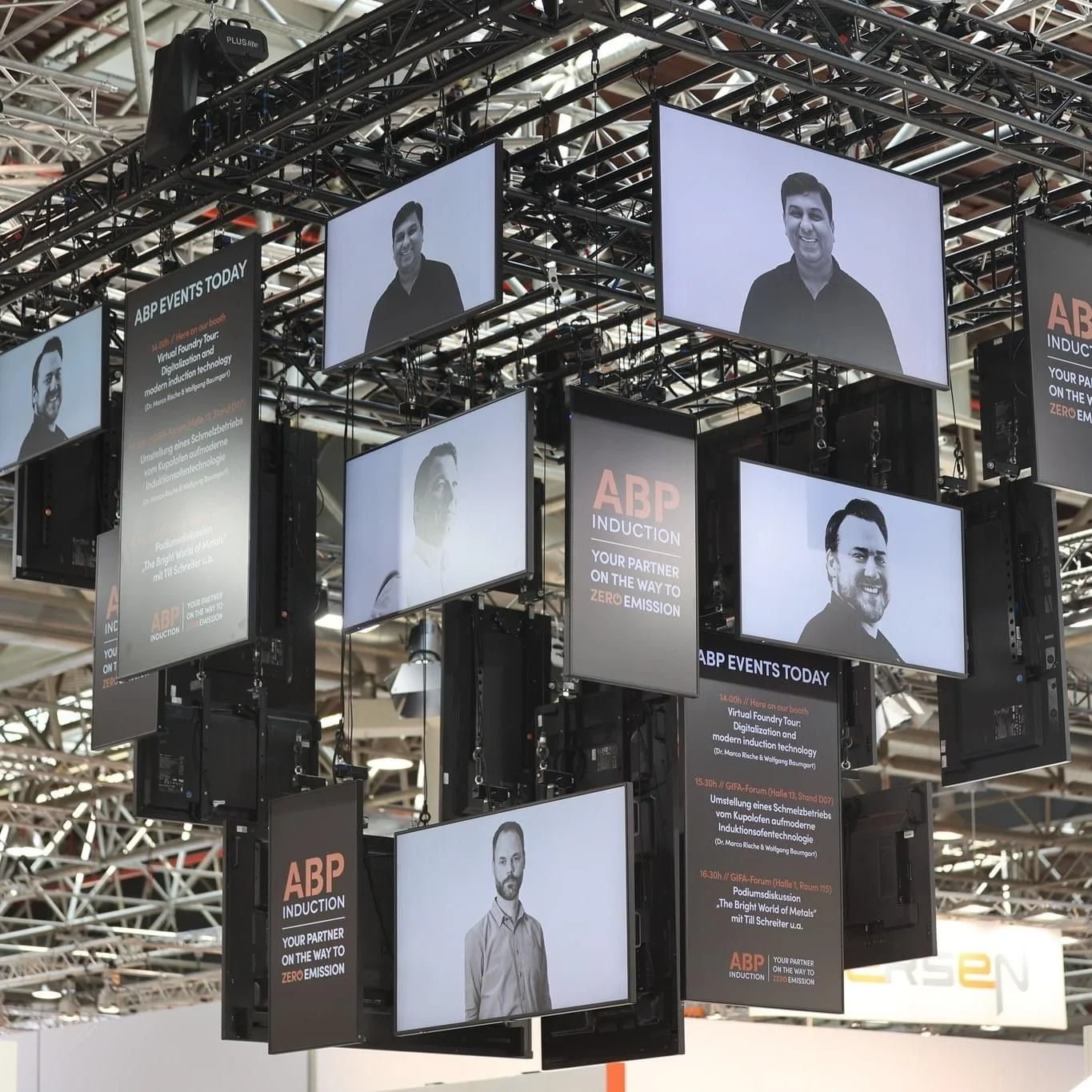 Multiple screens displaying speakers at an event with signs promoting ABP induction and zero emissions.