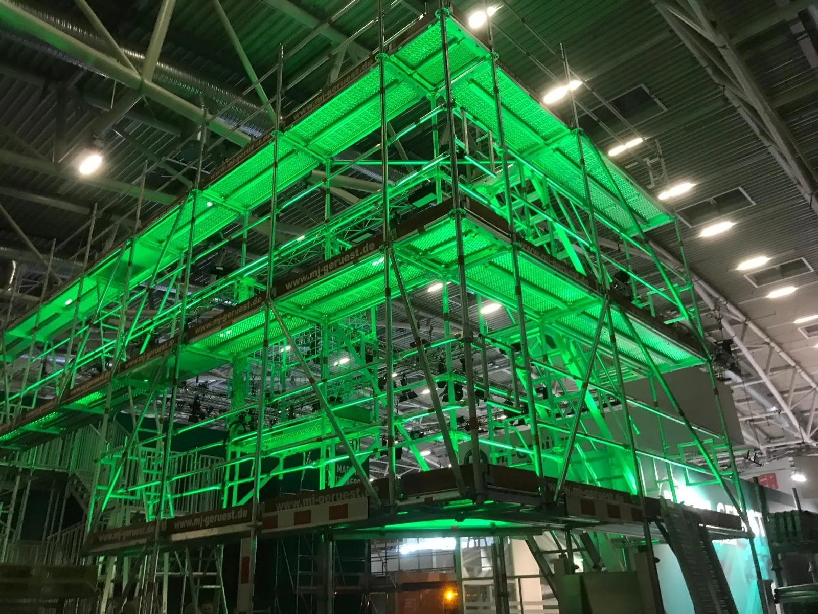 Green illuminated scaffolding structure inside a building, likely for construction or display setup.