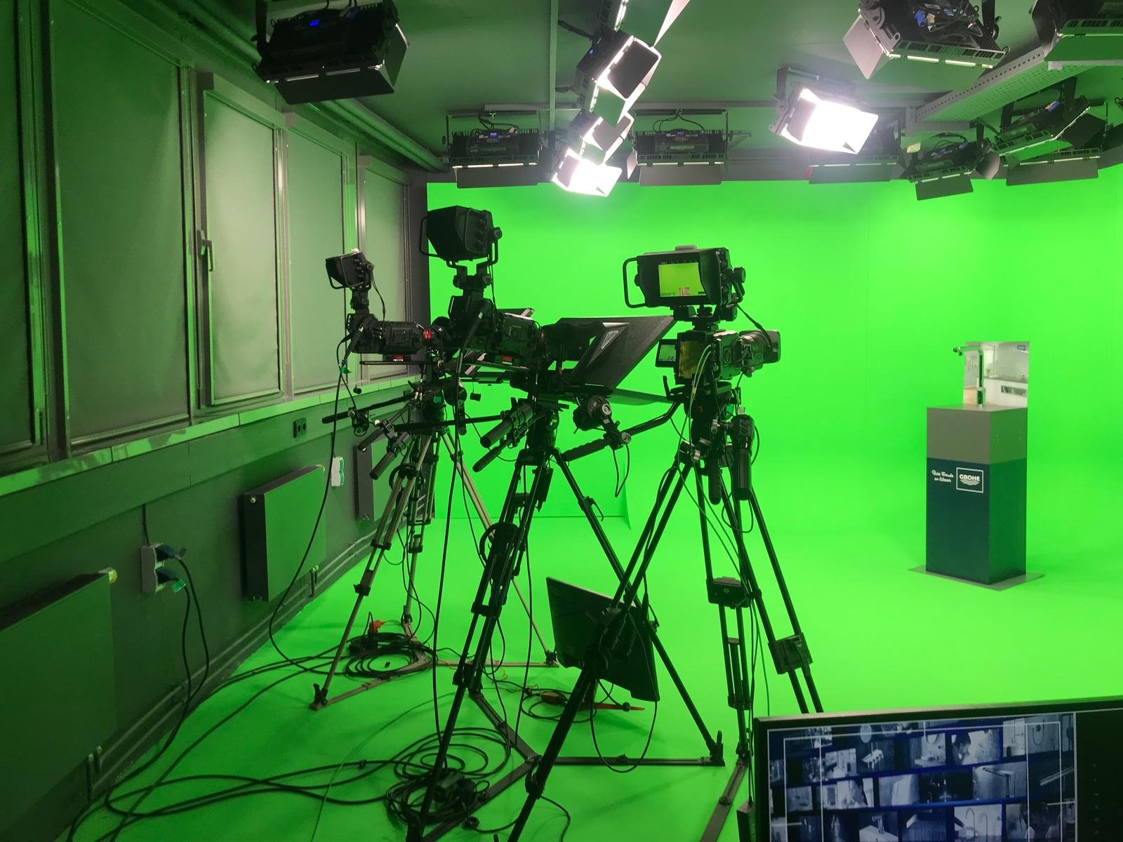 A professional photography or video studio with multiple camera equipment and lights in front of a green chroma key backdrop used for video production or broadcasting.