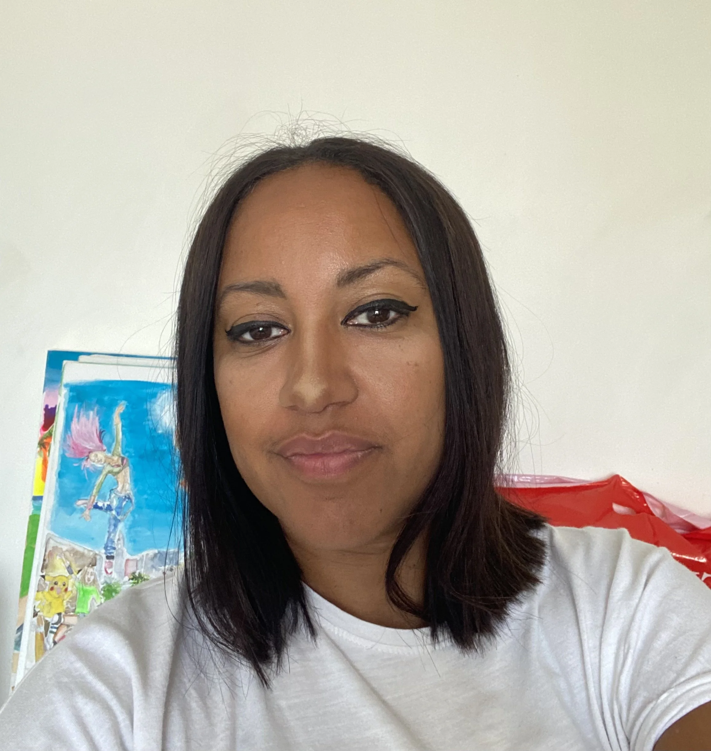 Portrait d'une femme avec des cheveux mi-longs, maquillage avec eyeliner noir, vêtue d'un t-shirt blanc, en intérieur, avec une œuvre d'art colorée en arrière-plan.