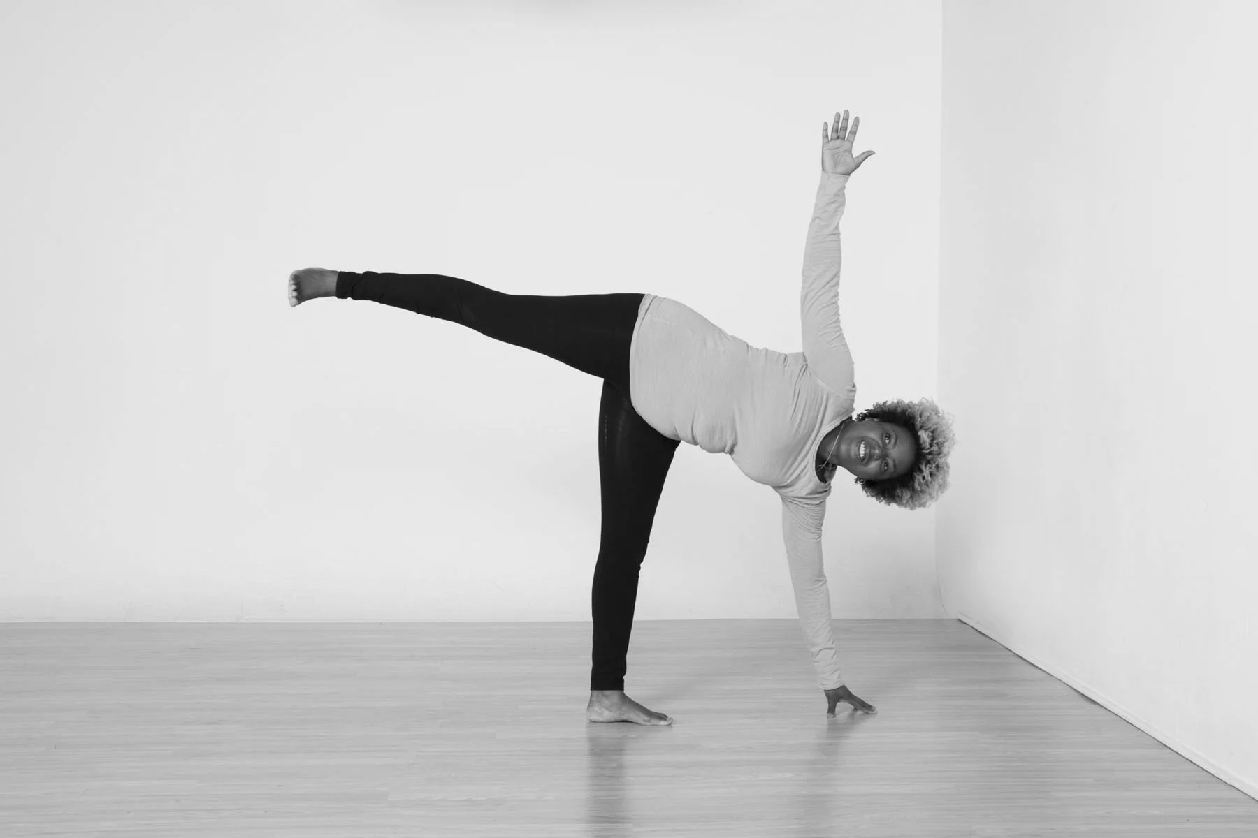 A person doing a one-handed side plank yoga pose in a minimalist room with light-colored wood floor.