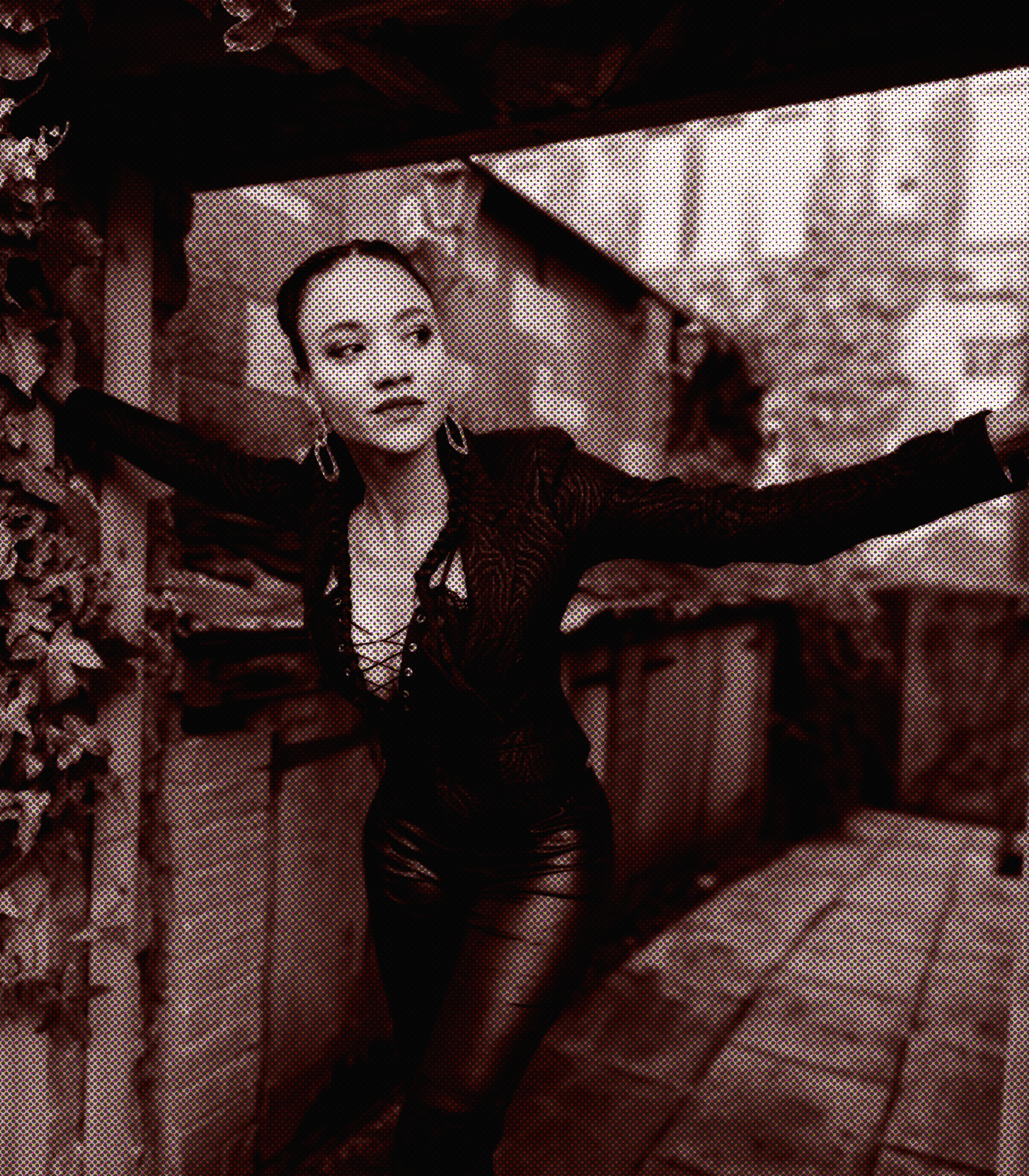 A person with tied hair and earrings, with both arm raised above their head, standing outdoors.