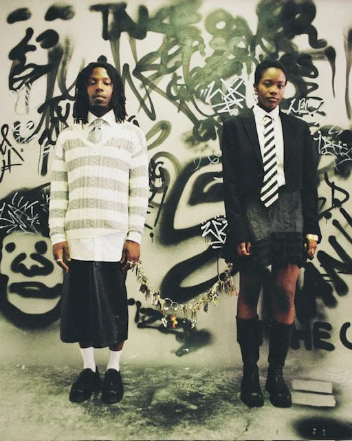 Two young women standing in front of a graffiti-covered wall.