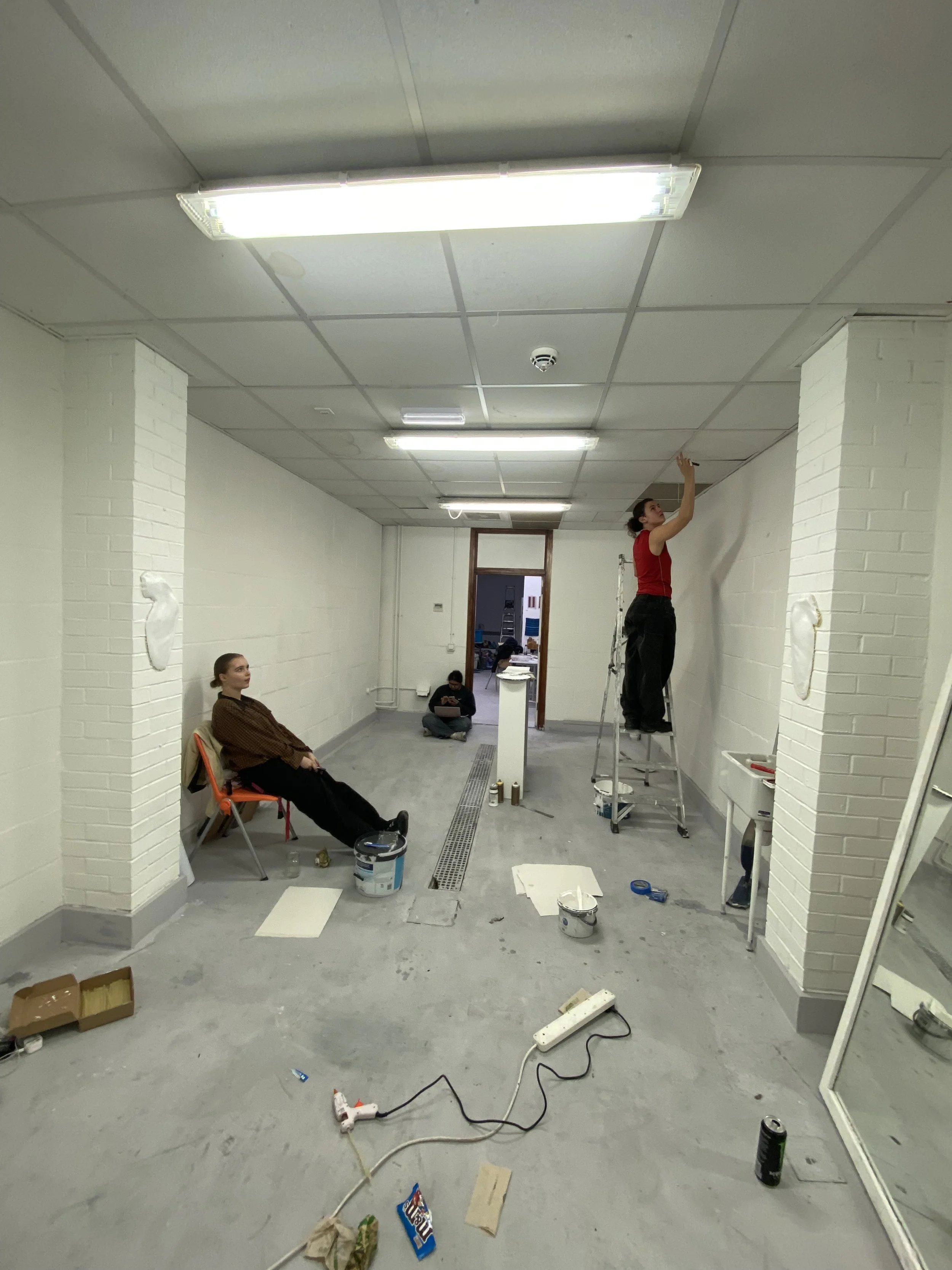 People working on painting or renovation in a room with white brick walls and fluorescent ceiling lights.