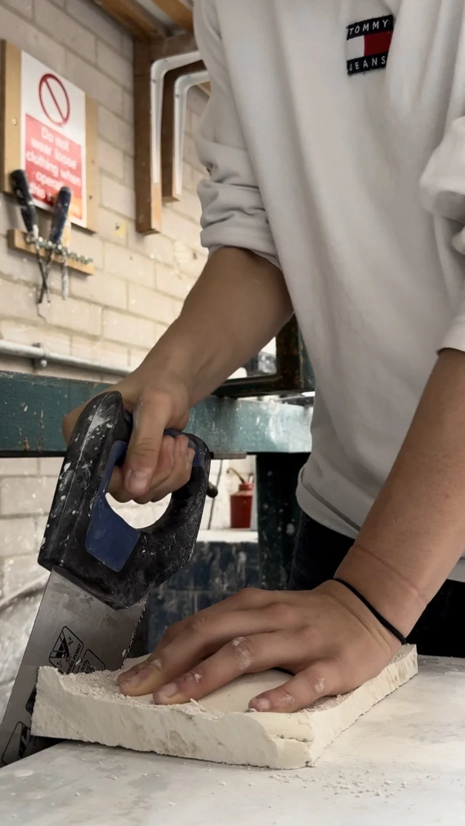 Person sawing a piece of wood in a workshop.