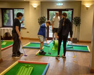 People playing mini golf indoors with artificial greens and snakes on the floor.
