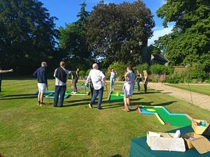 People playing mini-golf on an outdoor course with green grass and trees in the background.
