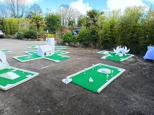 Miniature golf course with several holes, featuring cartoonish animal and nature-themed decorations, set outdoors on a sunny day.