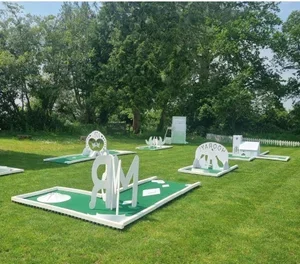 Miniature golf course with artificial grass, featuring various themed obstacles and structures, surrounded by trees and a white picket fence.