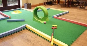 Miniature golf course with a green, a ramp, and obstacles inside a room.