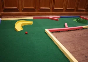 Indoor miniature golf course with colorful obstacles and a ball on the green.