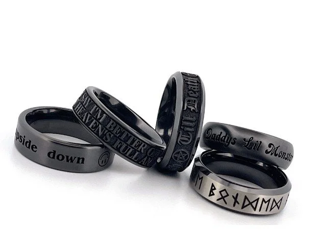 Five black and gray rings with engraved or embossed text and symbols, arranged in a semi-circle.