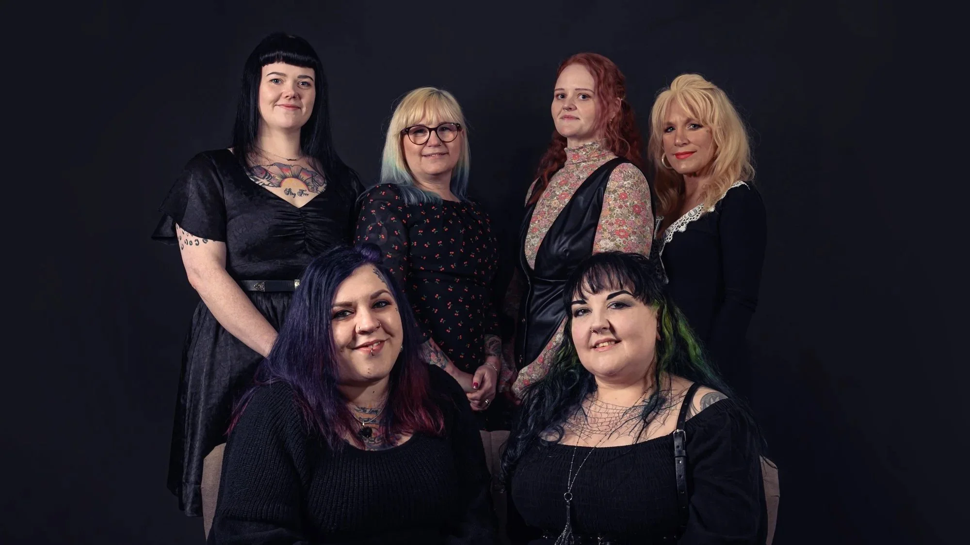 Six women posing against a black background, with diverse hairstyles, clothing, and hairstyles, smiling and looking at the camera.