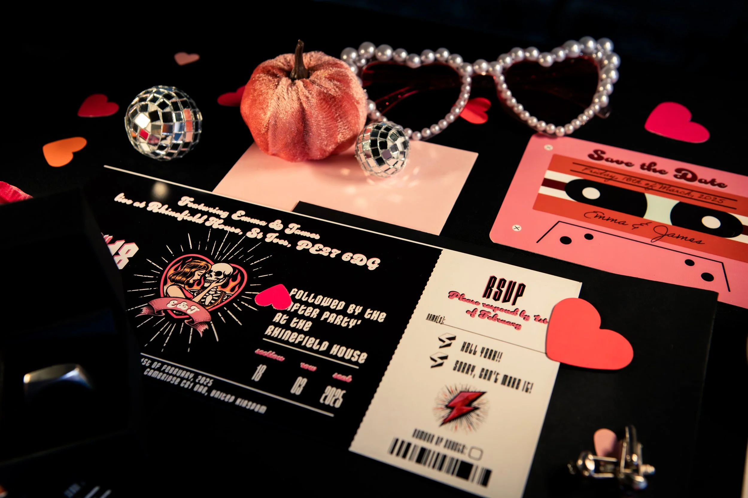 Valentine's Day themed party invites, accessories, and decorations, including a velvet pumpkin, pearl necklace, disco ball ornaments, and heart-shaped confetti on a black background.