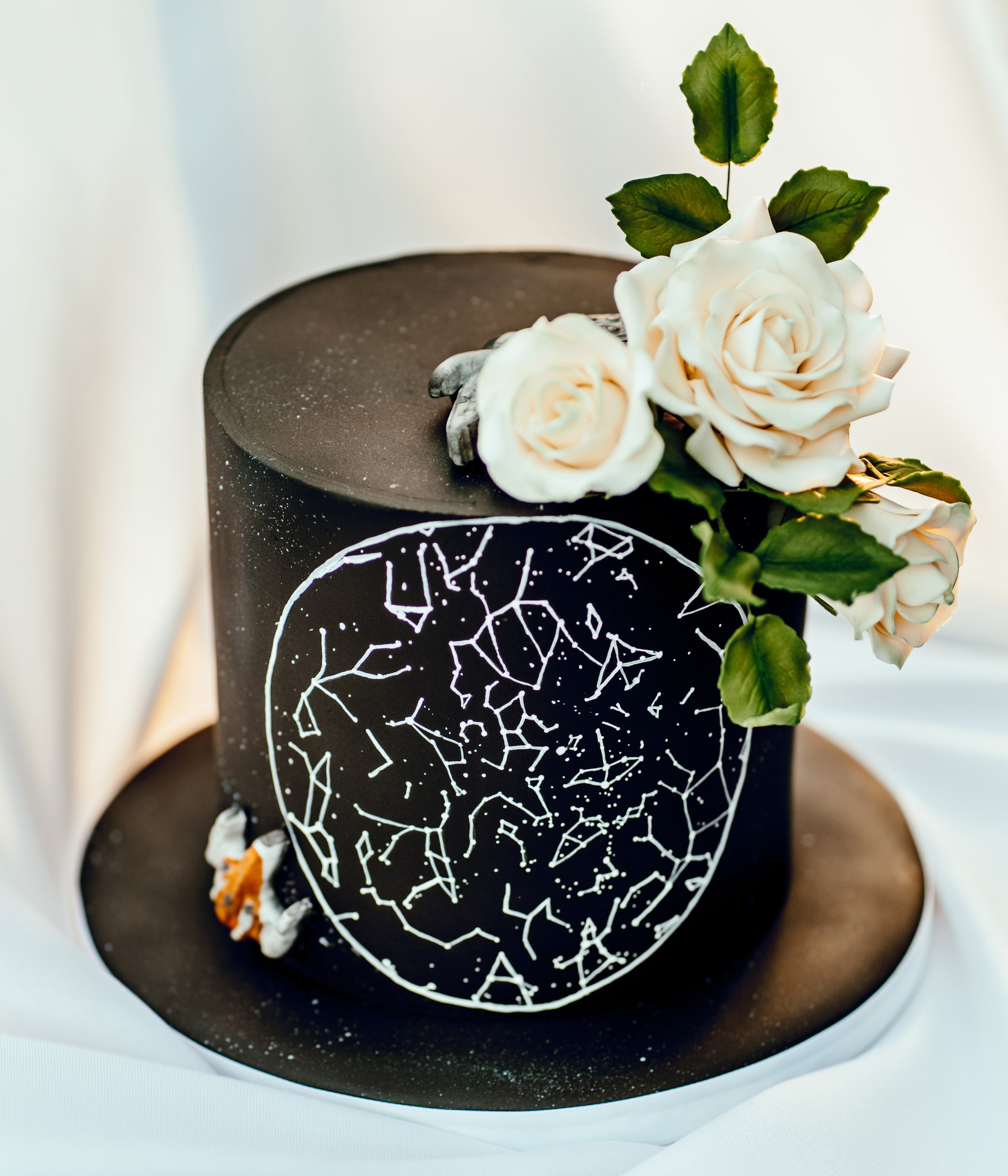 A black wedding cake with white constellation pattern and white roses on top.