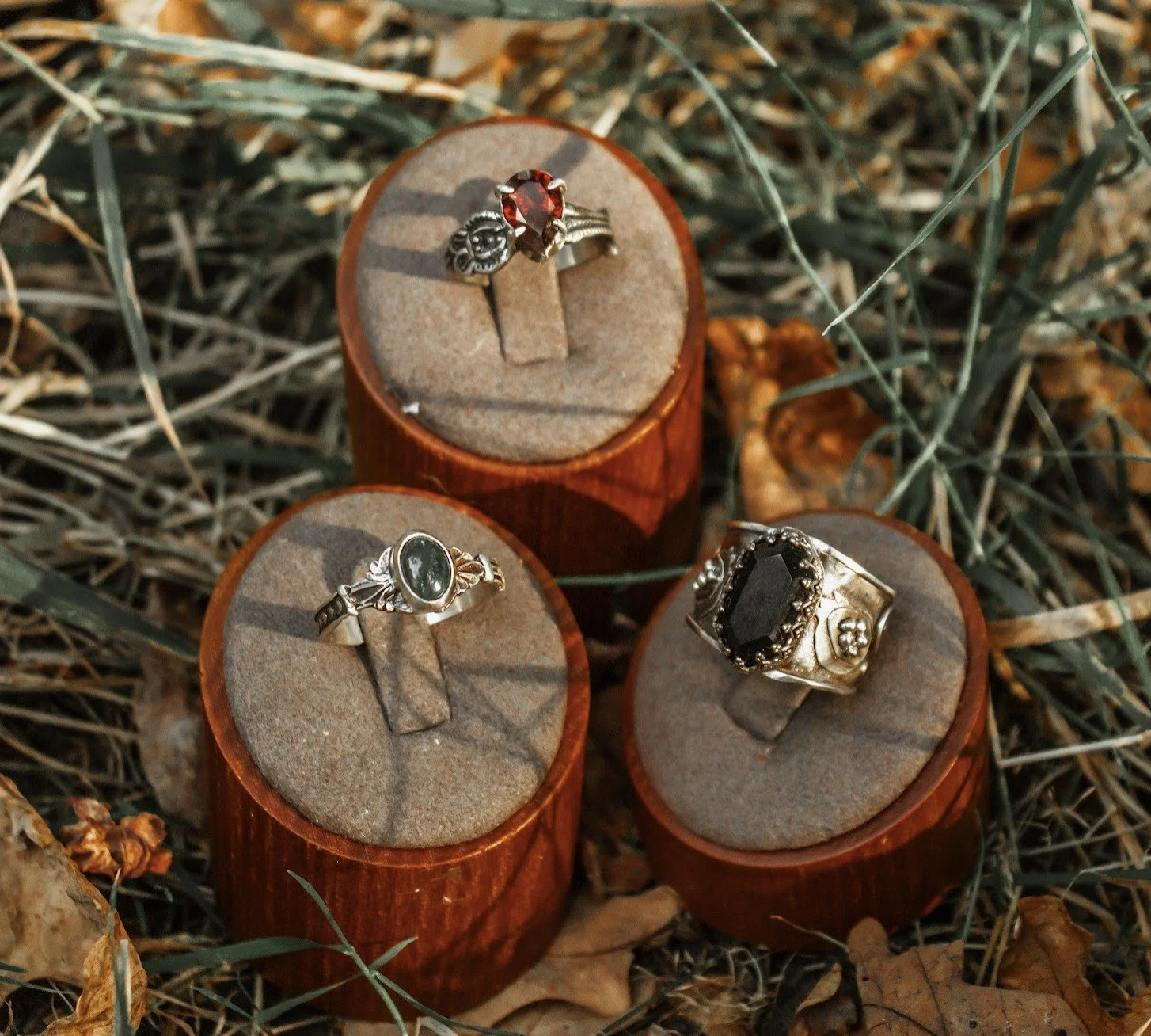 Three rings displayed on small wooden stands placed on a bed of dry grass and leaves.