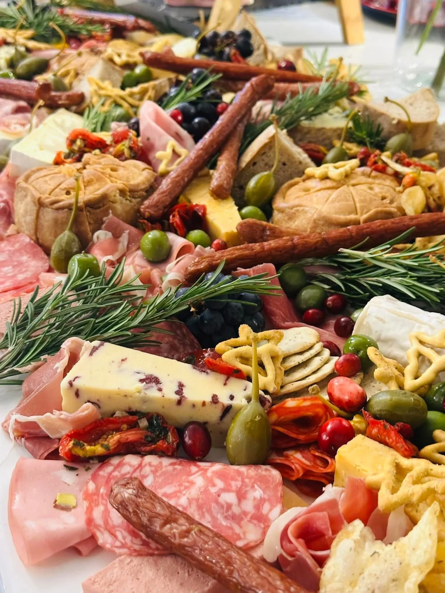 Close-up of a charcuterie board with assorted cheeses, cured meats, olives, bread, herbs, crackers, dried fruits, and nuts.