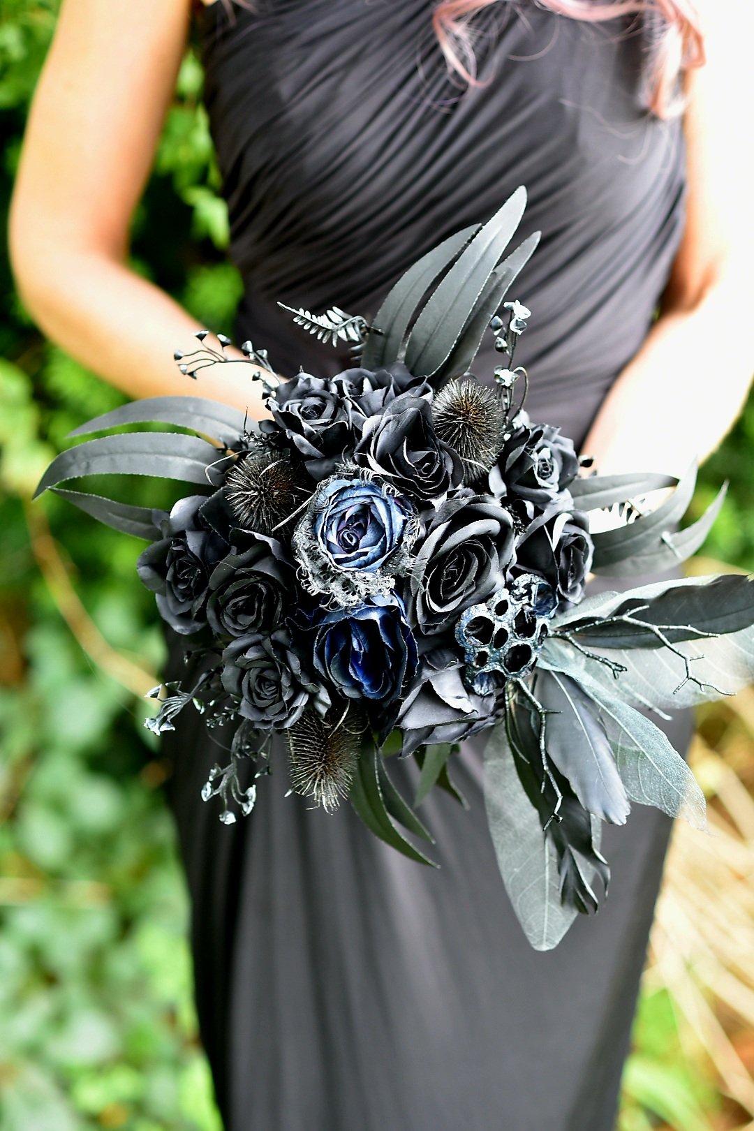 Woman in a dark gown holding a black and blue flower bouquet featuring roses and greenery.