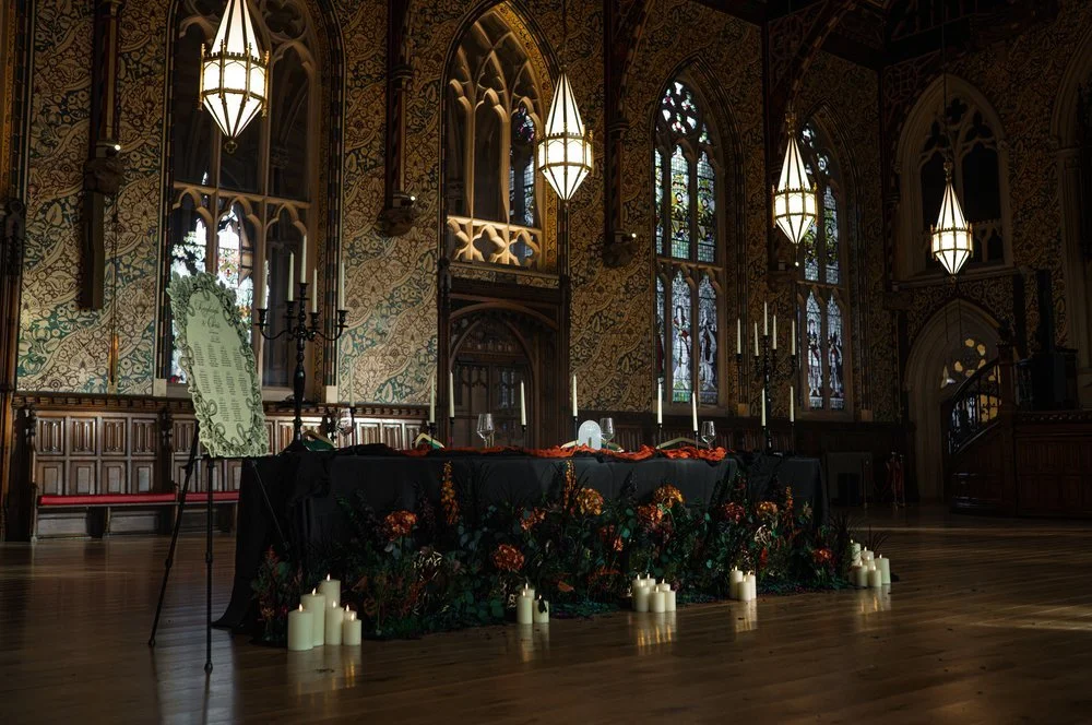 Interior of a decorated church with stained glass windows, ornate walls, hanging lanterns, and a table adorned with flowers, candles, and candelabras, likely set up for a wedding or special event.