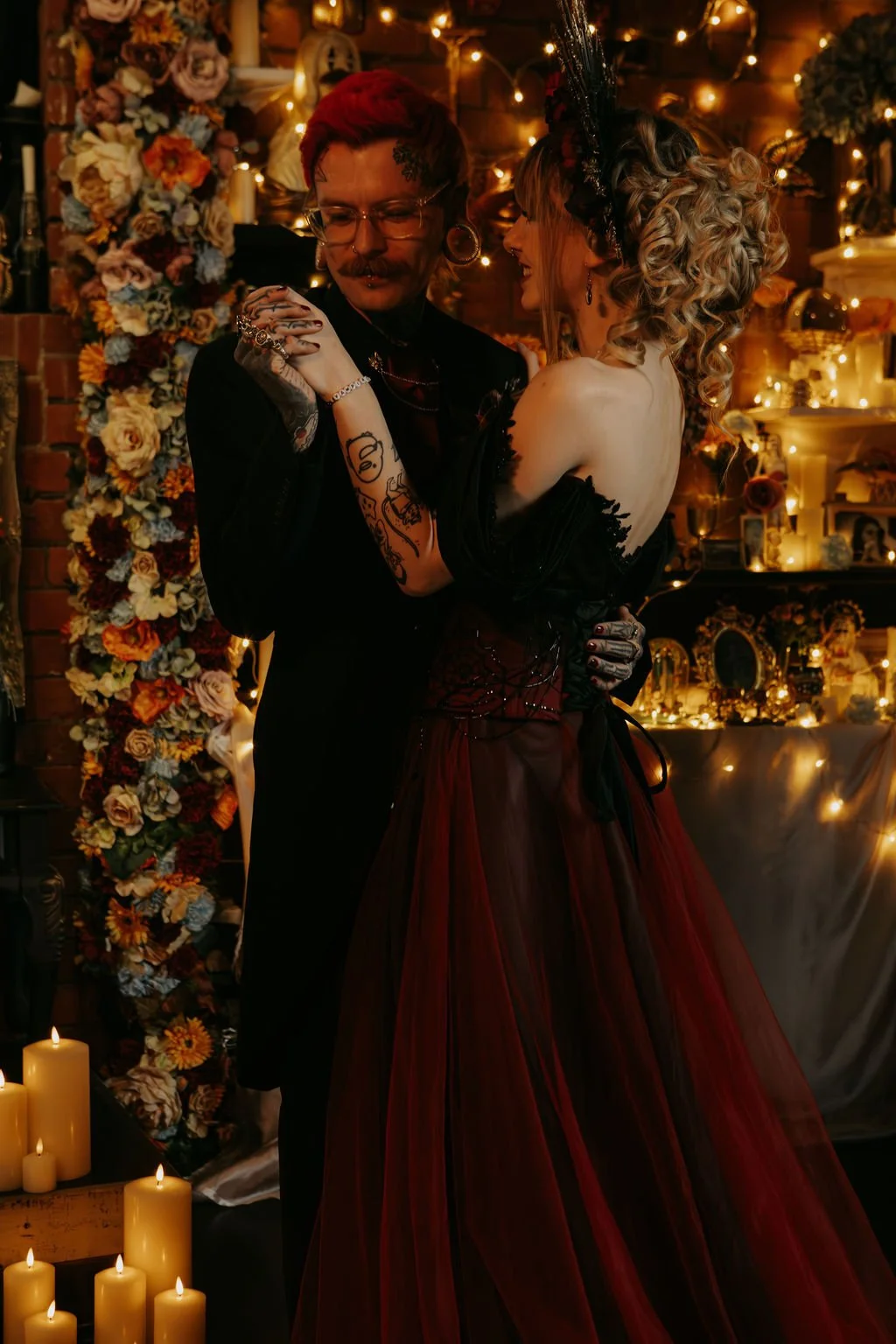 A couple dancing closely in a warmly lit, decorated room with candles, flowers, and fairy lights.