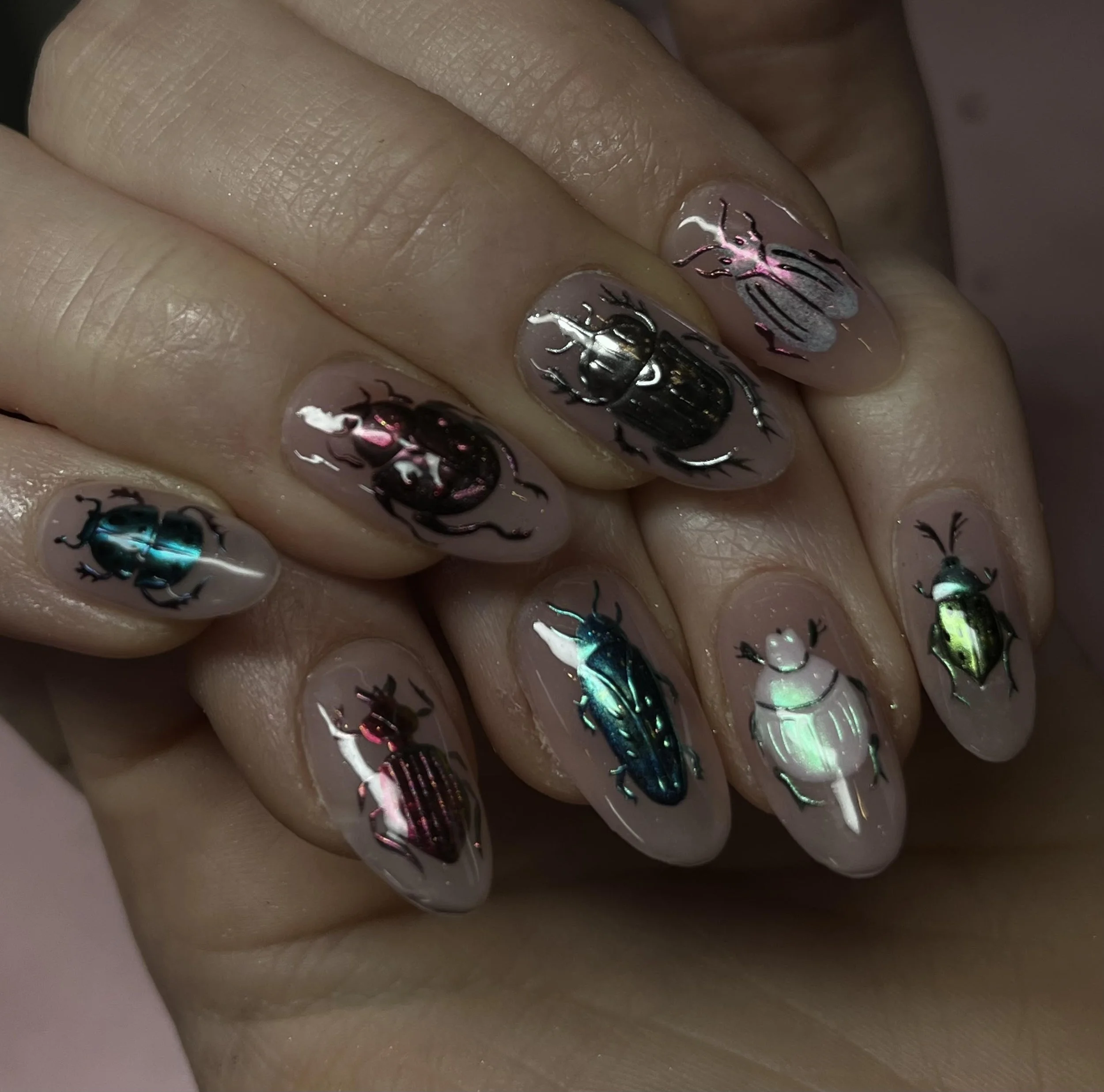 Nail art featuring holographic beetle designs in various colors on natural nail tips.