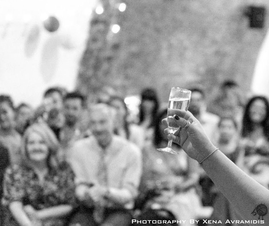 A person holding a champagne flute in front of a blurred crowd at a social gathering or celebration.