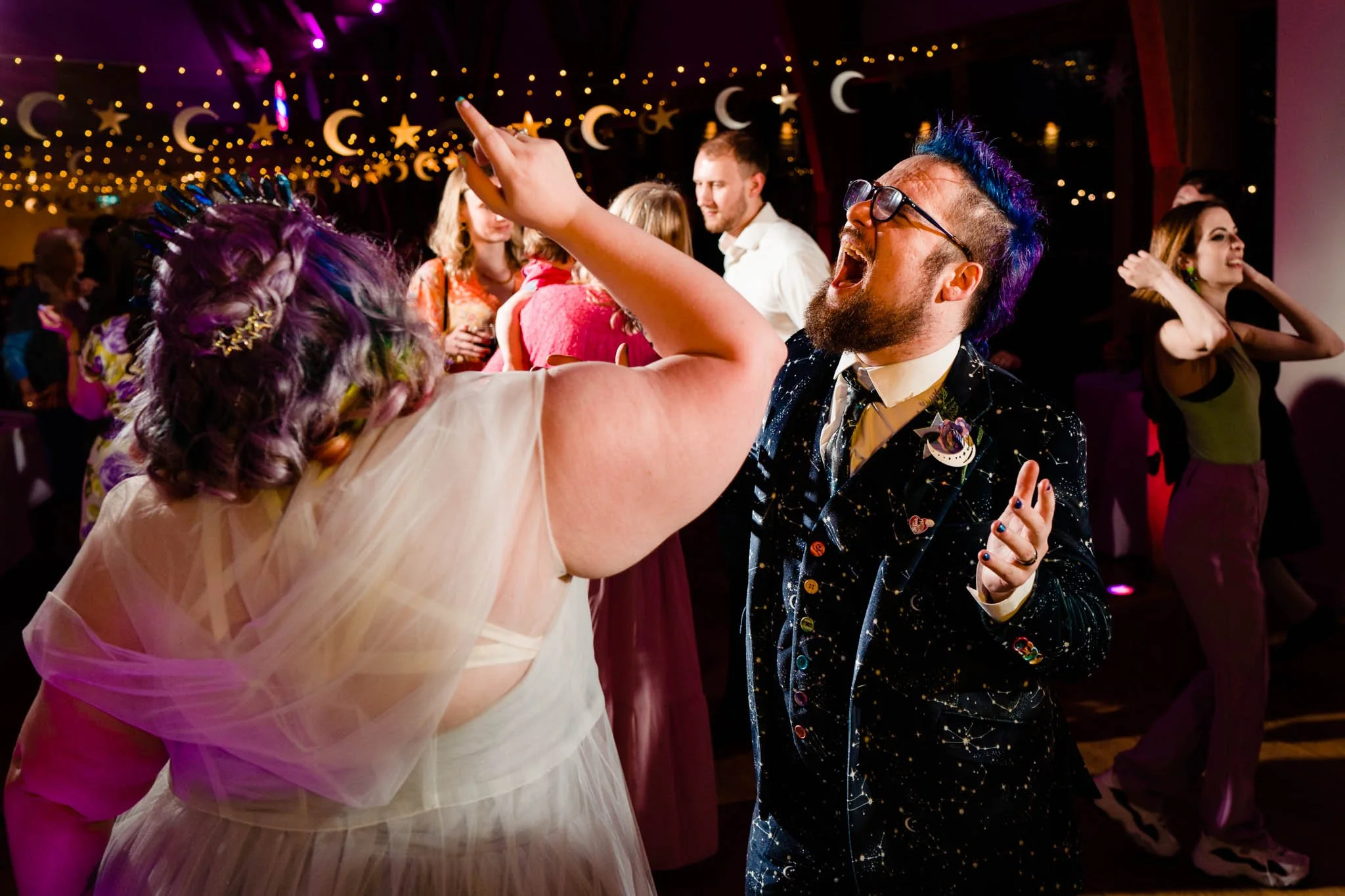People dancing at a party under moon and star decorations with colorful lights.