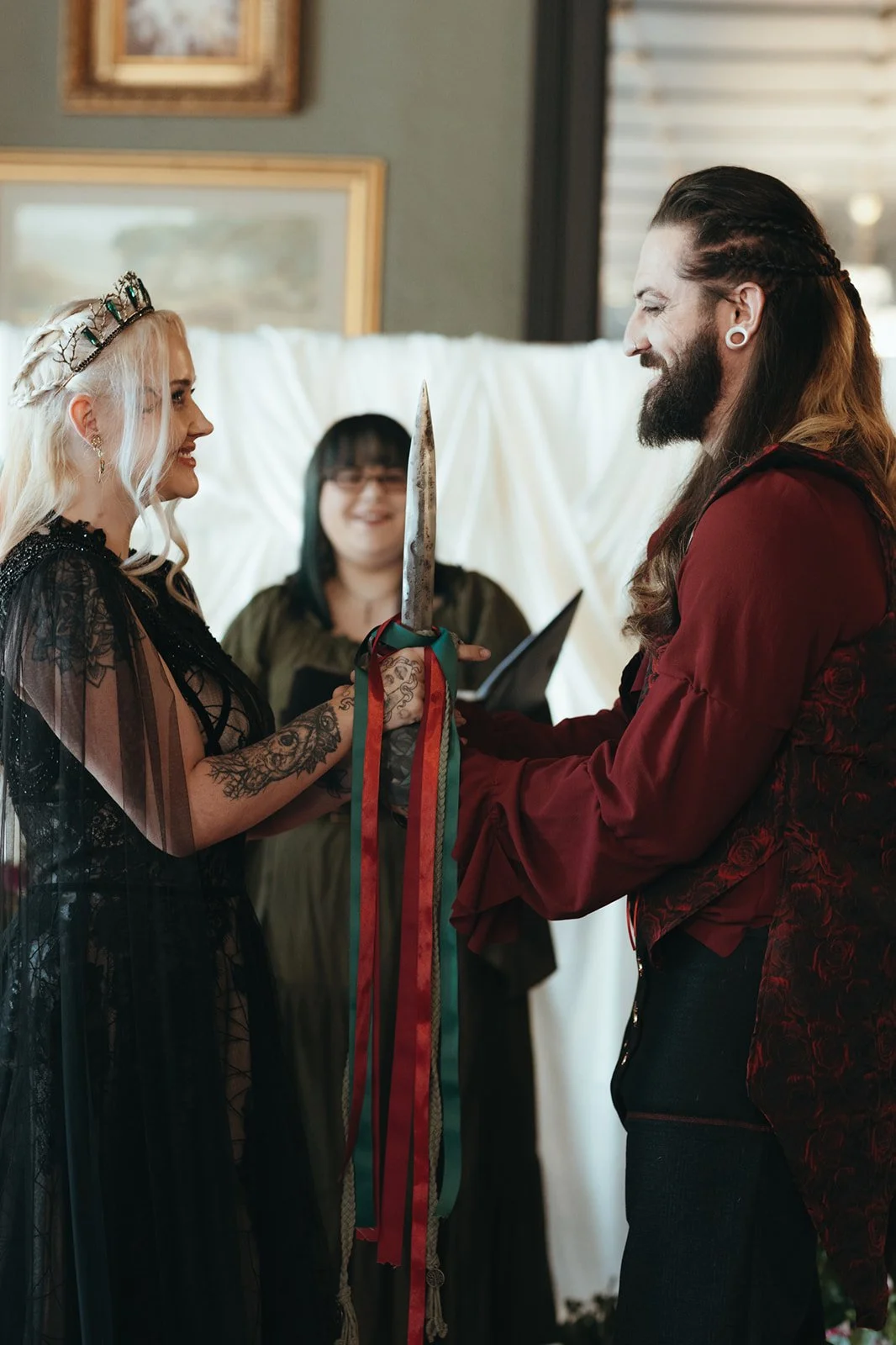 A couple exchanging rings during a wedding ceremony with a woman officiant in the background, holding a book and smiling.
