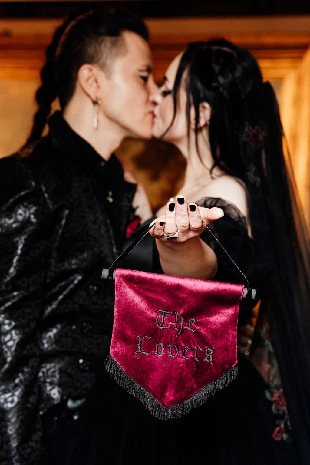 Two women kissing with a pink velvet bag reading 'The Lovers' in the foreground