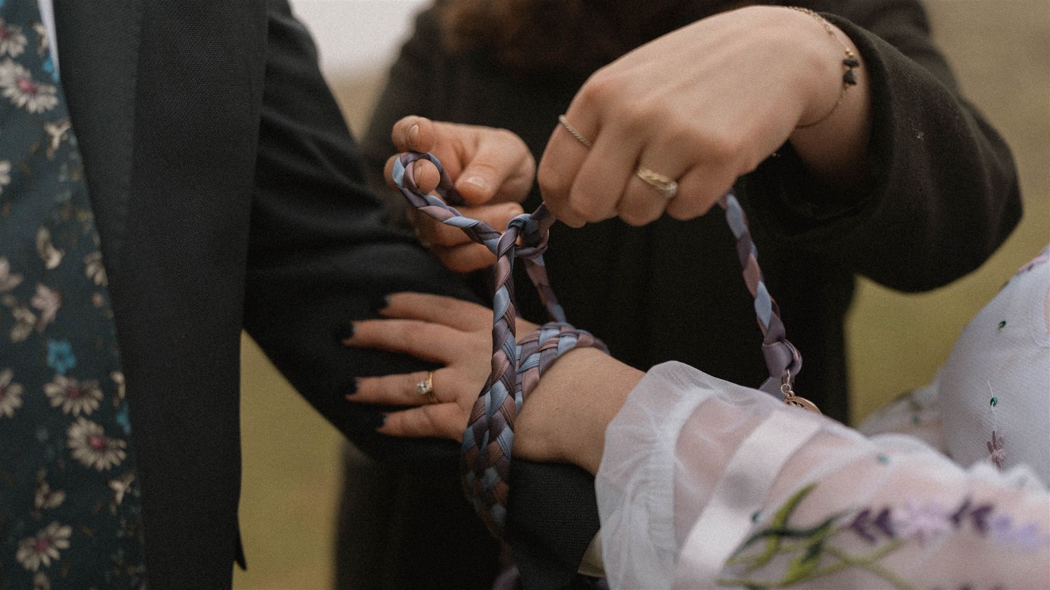 Close-up of two individuals tying braided fabric bracelets around each other's wrists during a ceremony or ritual.
