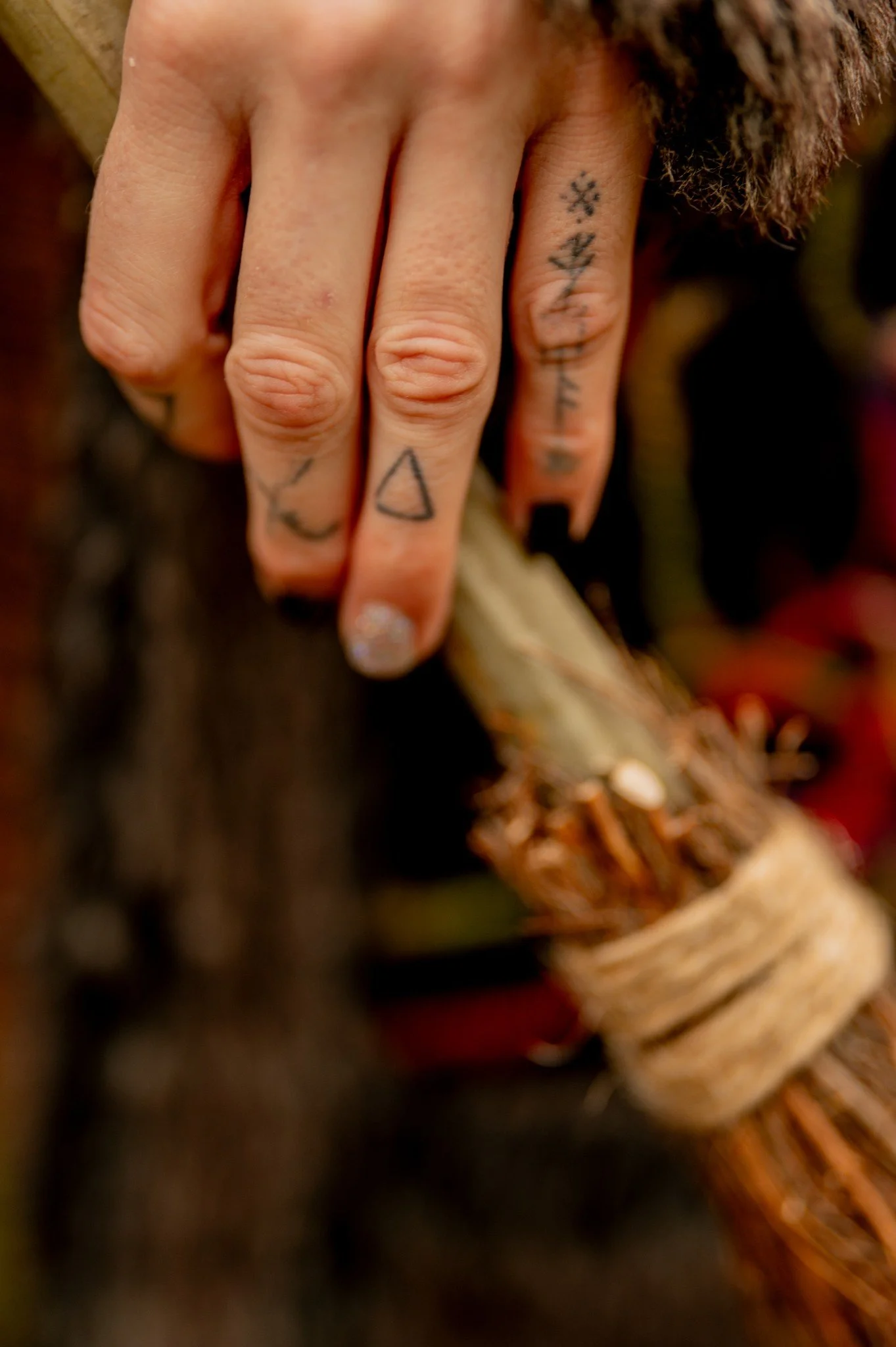 Close-up of a person's hand with several small tattoos on the fingers, including geometric shapes, on a blurred background.