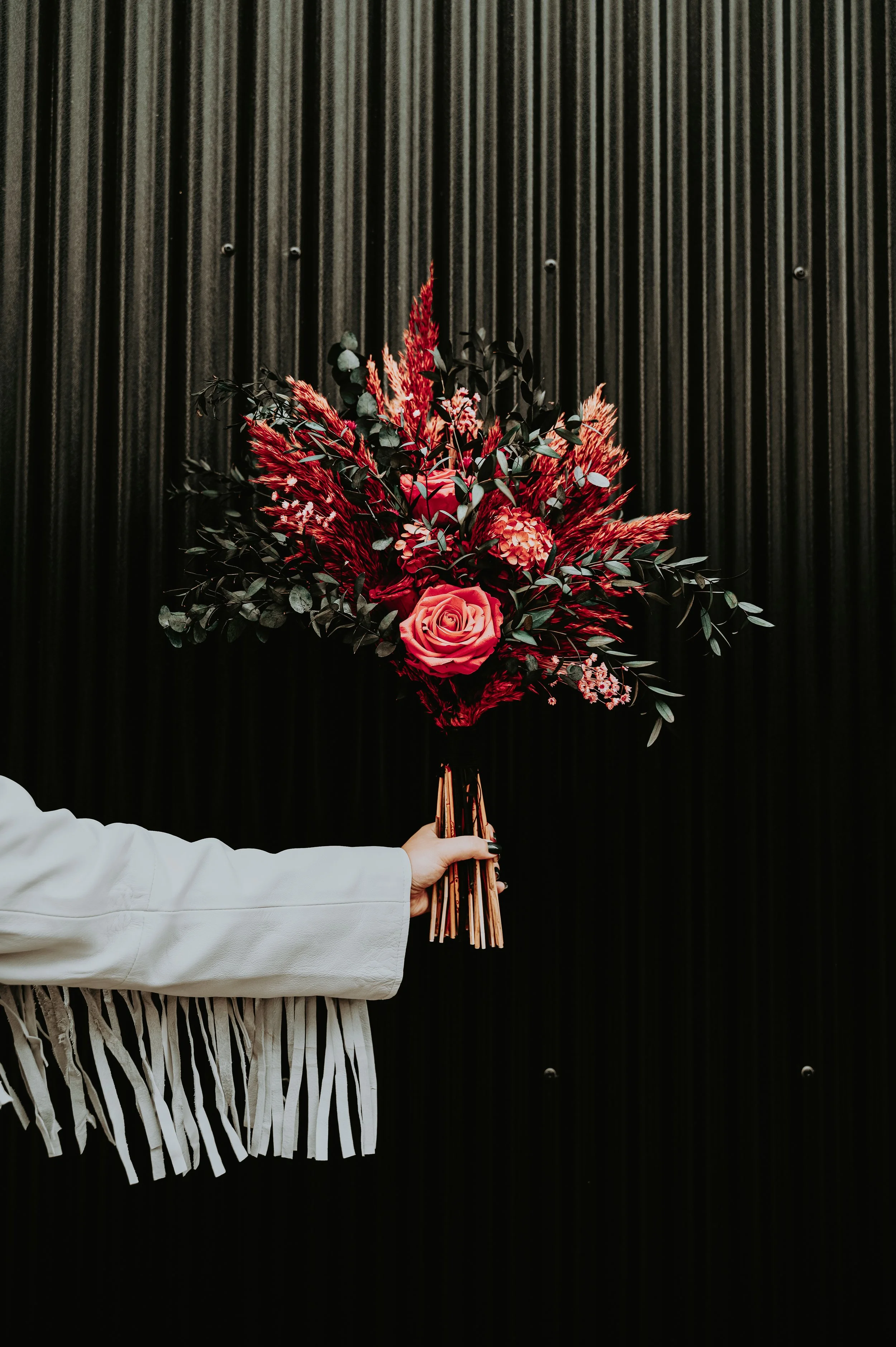 A person's hand holding a bouquet of red and pink flowers against a black ribbed background.