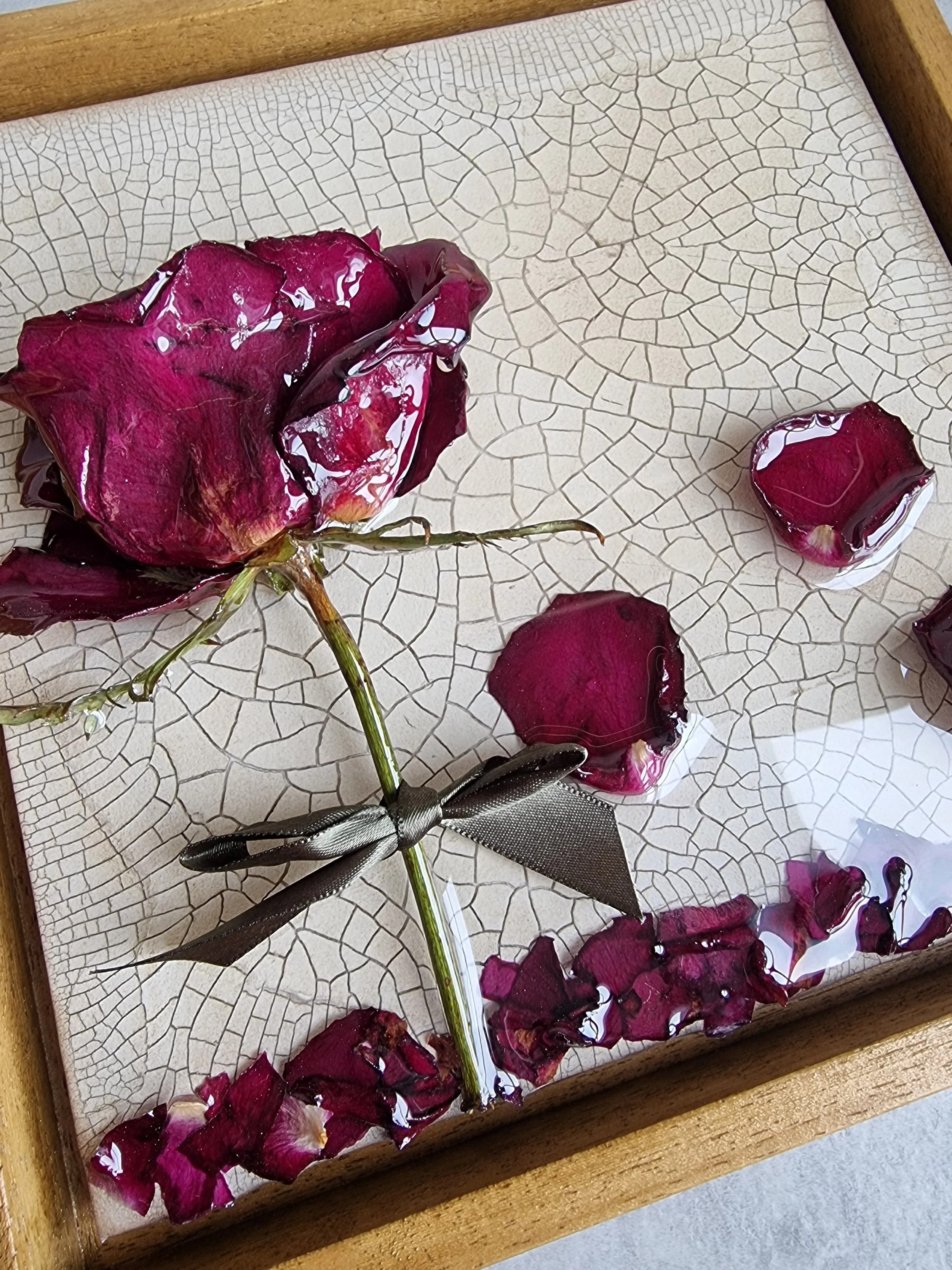 A floral arrangement with dried red rose petals and a whole dried rose in a wooden box with a crackle finish.