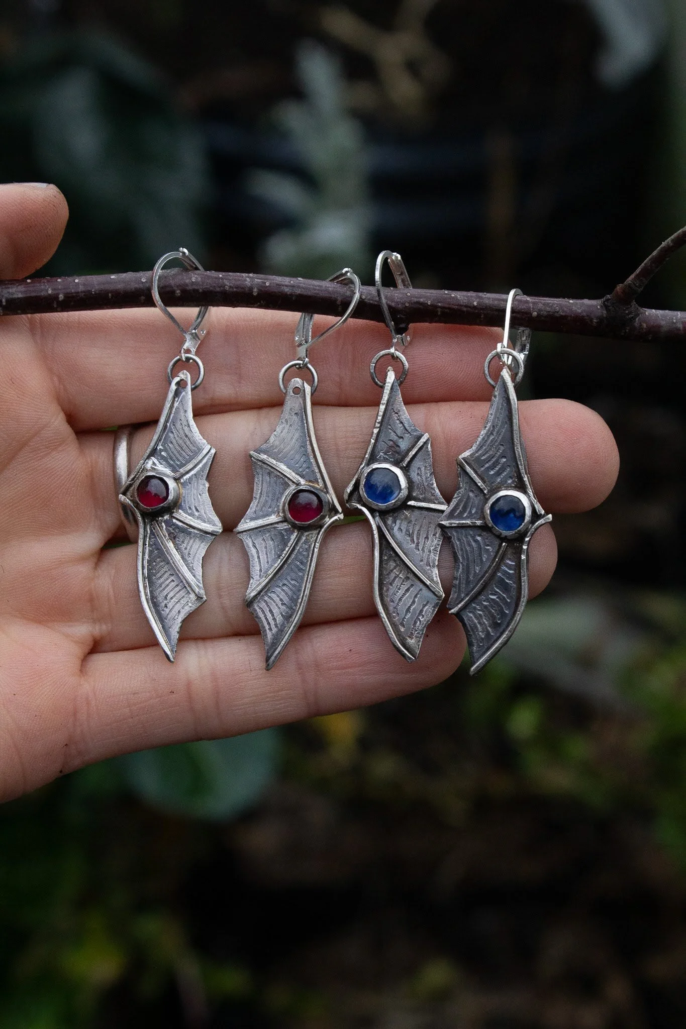Pair of silver earrings designed to resemble bat wings, with red and blue gemstones in the center.