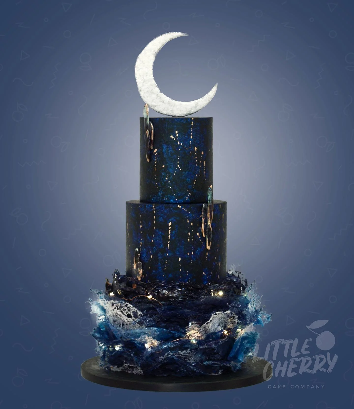 A three-tiered cake with a celestial theme, decorated in dark blue with gold star-like accents, topped with a white crescent moon, and set on a base with blue and black textured decorations resembling ocean waves.