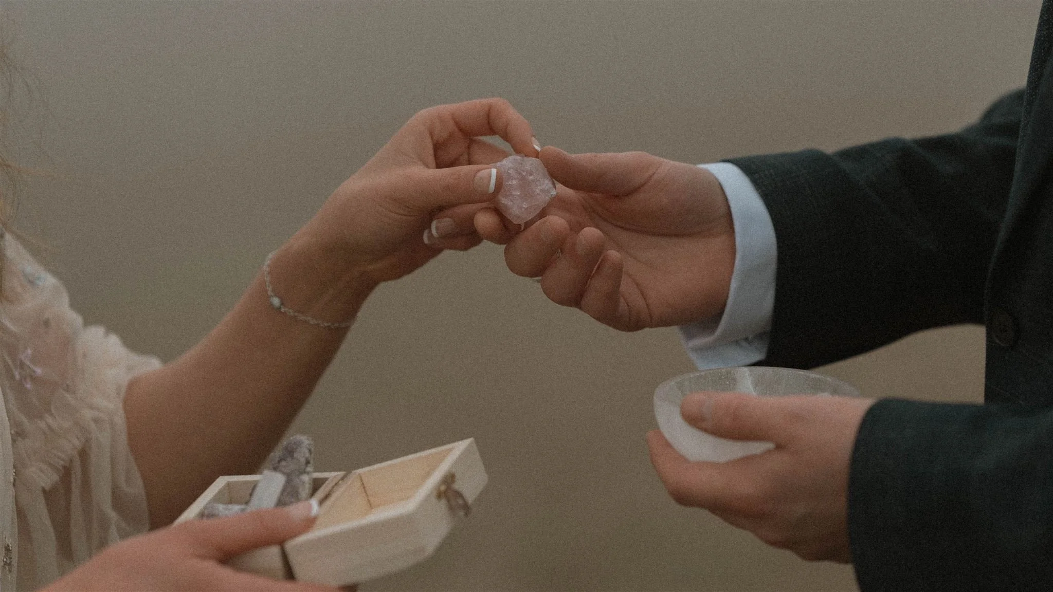 A woman and a man are exchanging a small rock at a wedding, with the woman holding a small box of jewelry and the man holding a small dish.
