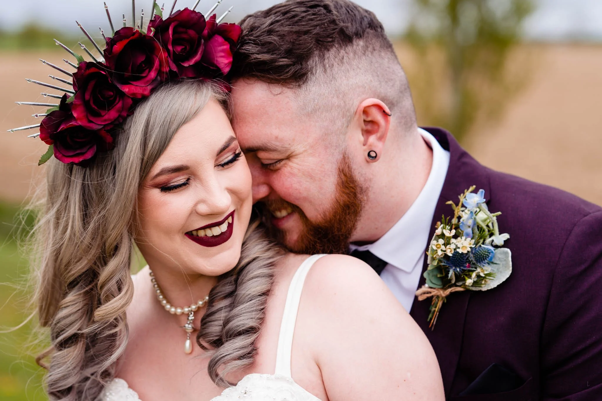 A bride and groom sharing a close, joyful moment outside on their wedding day, with their foreheads and noses touching, smiling and laughing.