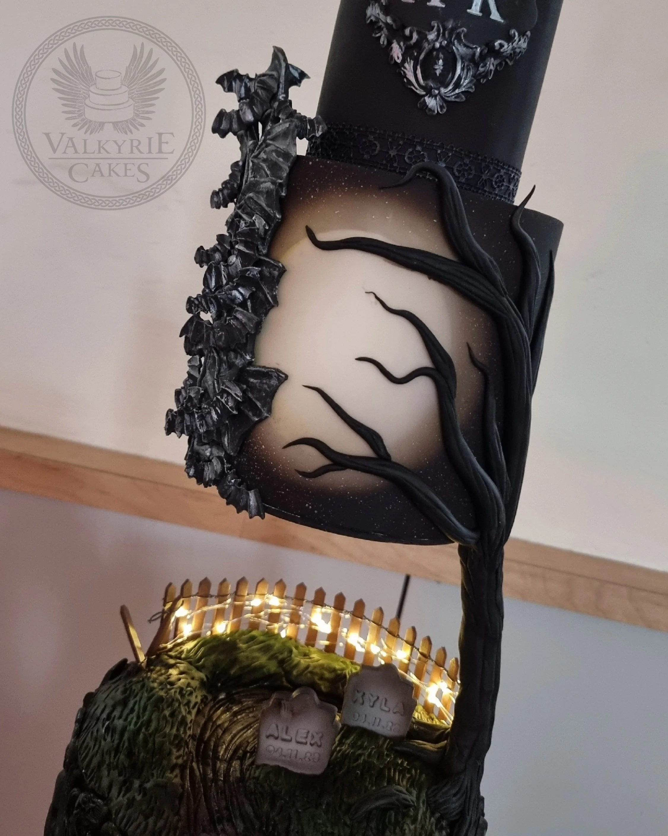 A Halloween-themed cake featuring a spookyc graveyard scene with a leafless black tree and a moonlit sky with stars.